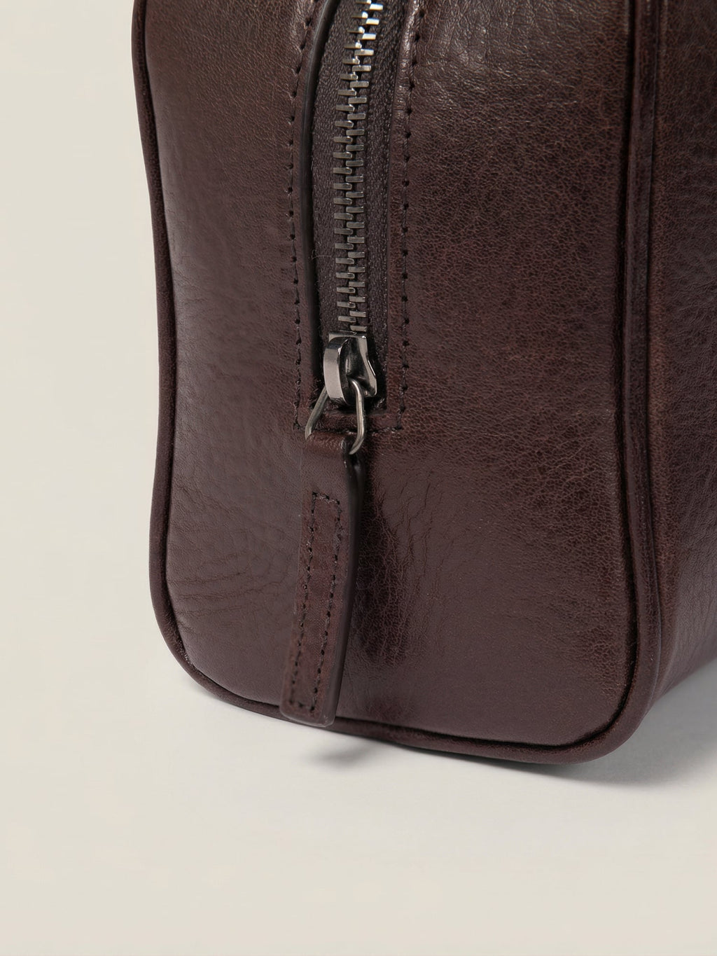 Chocolate brown full-grain leather wash bag detail showing the metal zipper and matching pull tab.