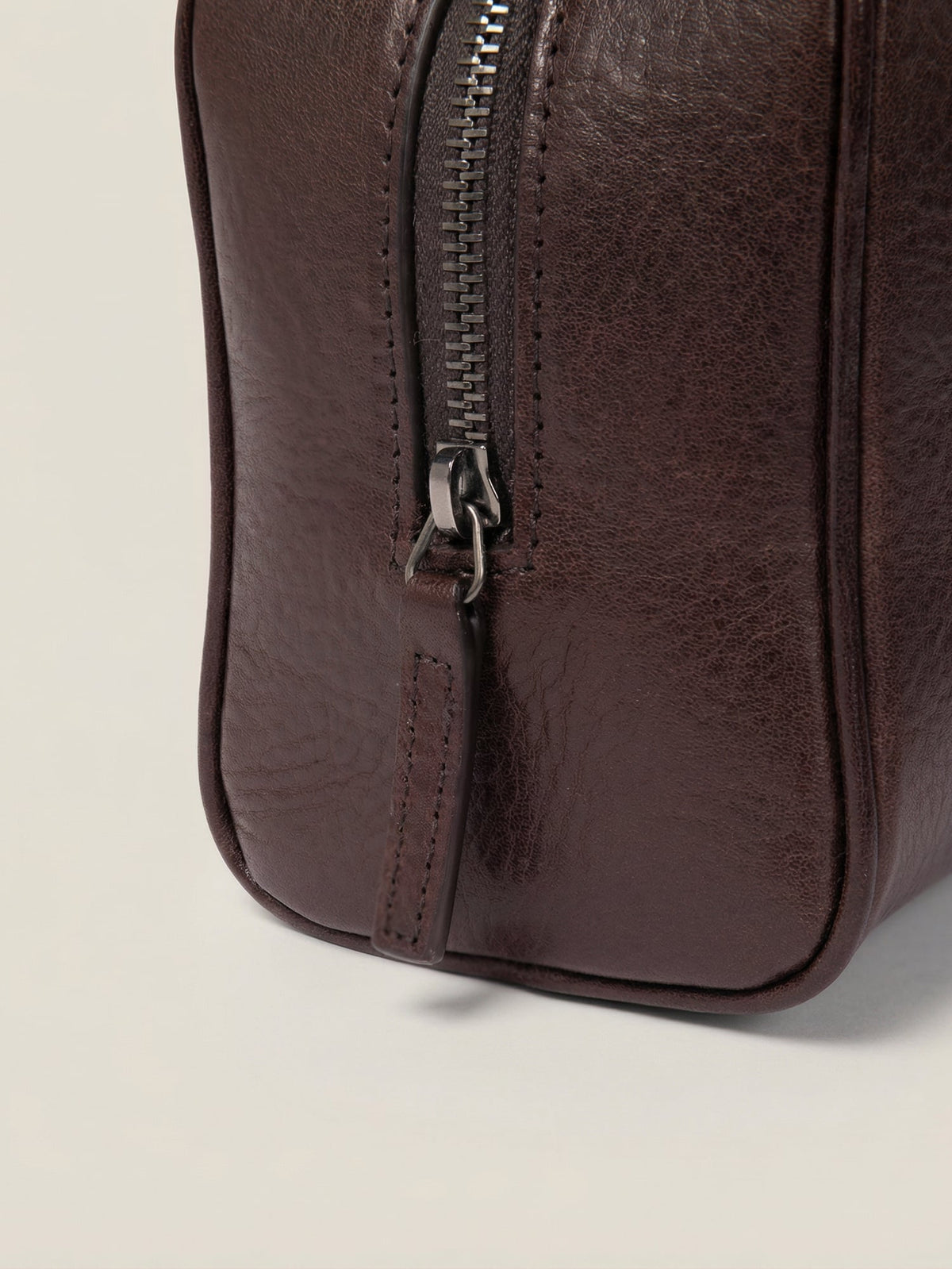 Chocolate brown full-grain leather wash bag detail showing the metal zipper and matching pull tab.