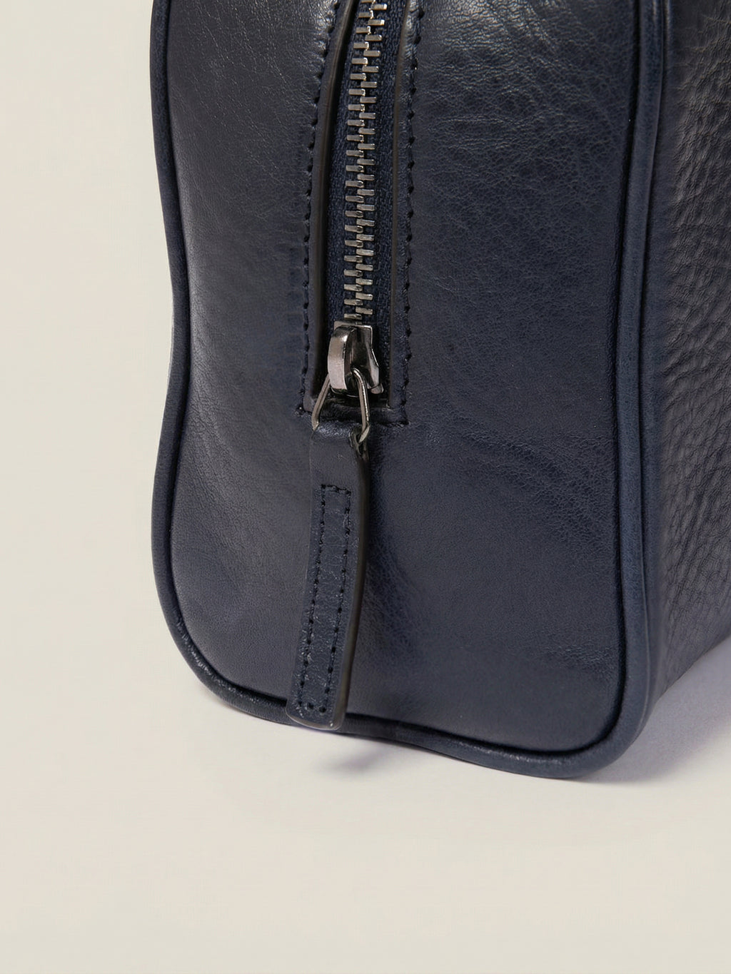 Detail view of the Ink Blue Leather Wash Bag, showing the zipper pull and textured full-grain calfskin leather.