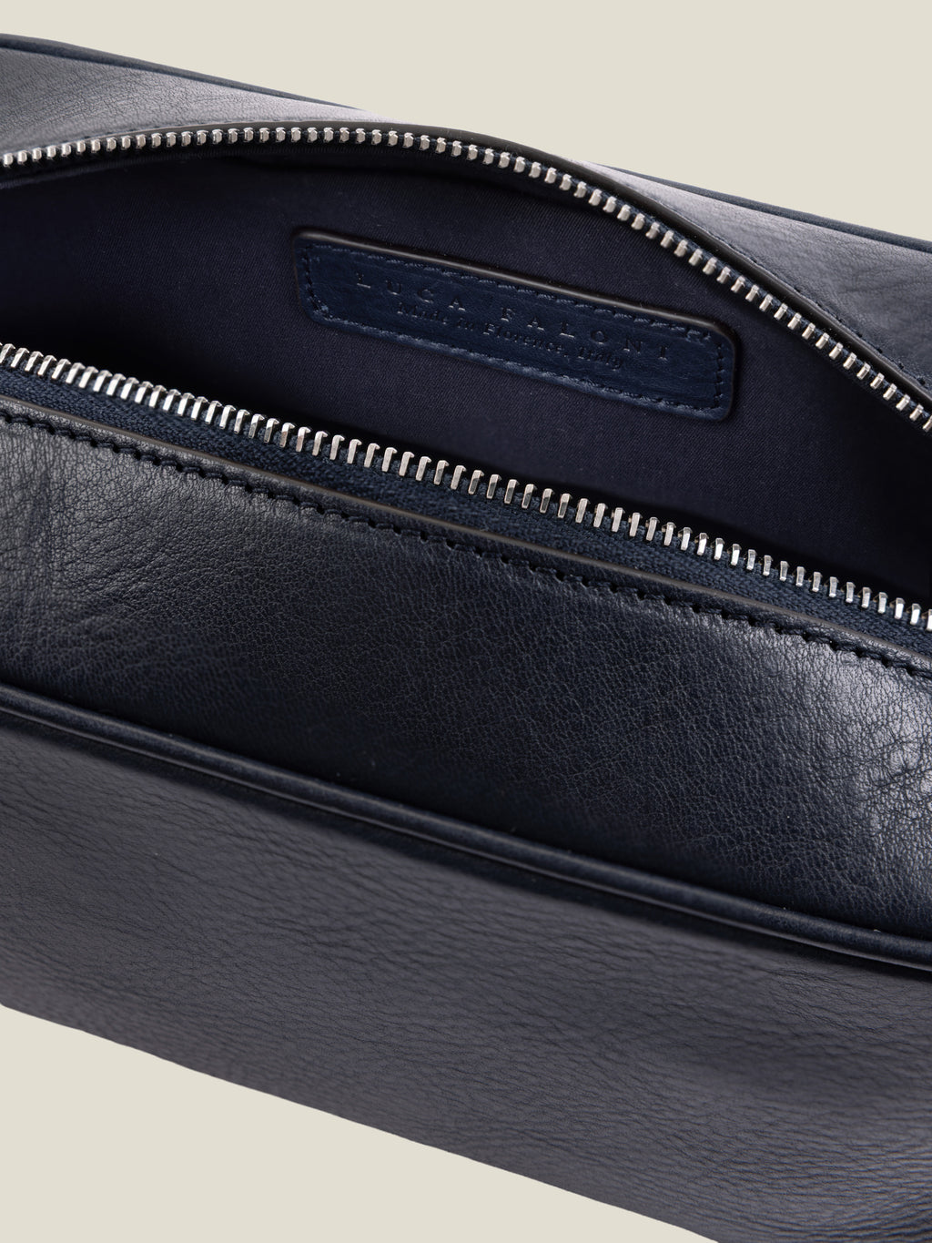 Detail of the ink blue full-grain leather wash bag, showcasing the open silver zipper and internal technical lining.