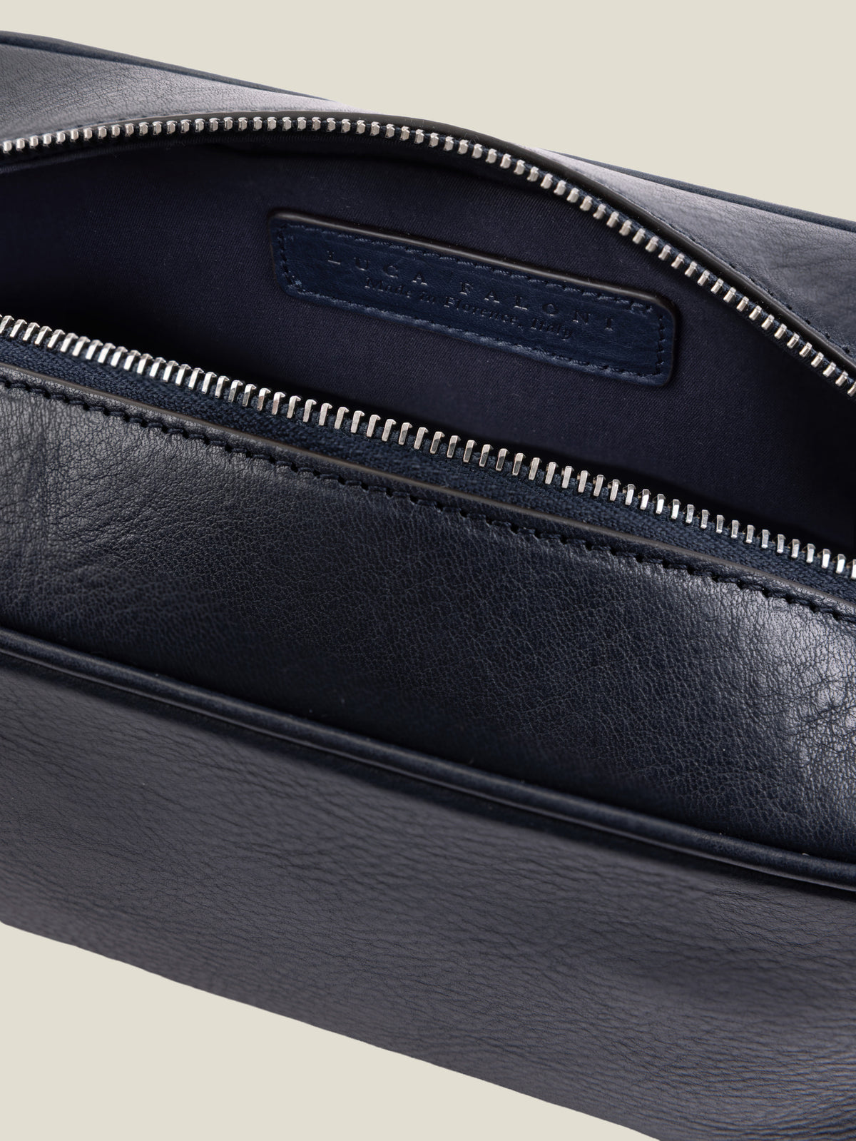 Detail of the ink blue full-grain leather wash bag, showcasing the open silver zipper and internal technical lining.