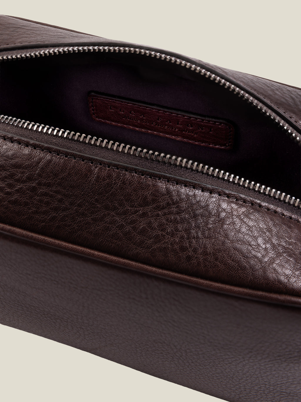 Close-up of the chocolate brown leather wash bag, showing the open silver zipper and water-resistant technical lining.