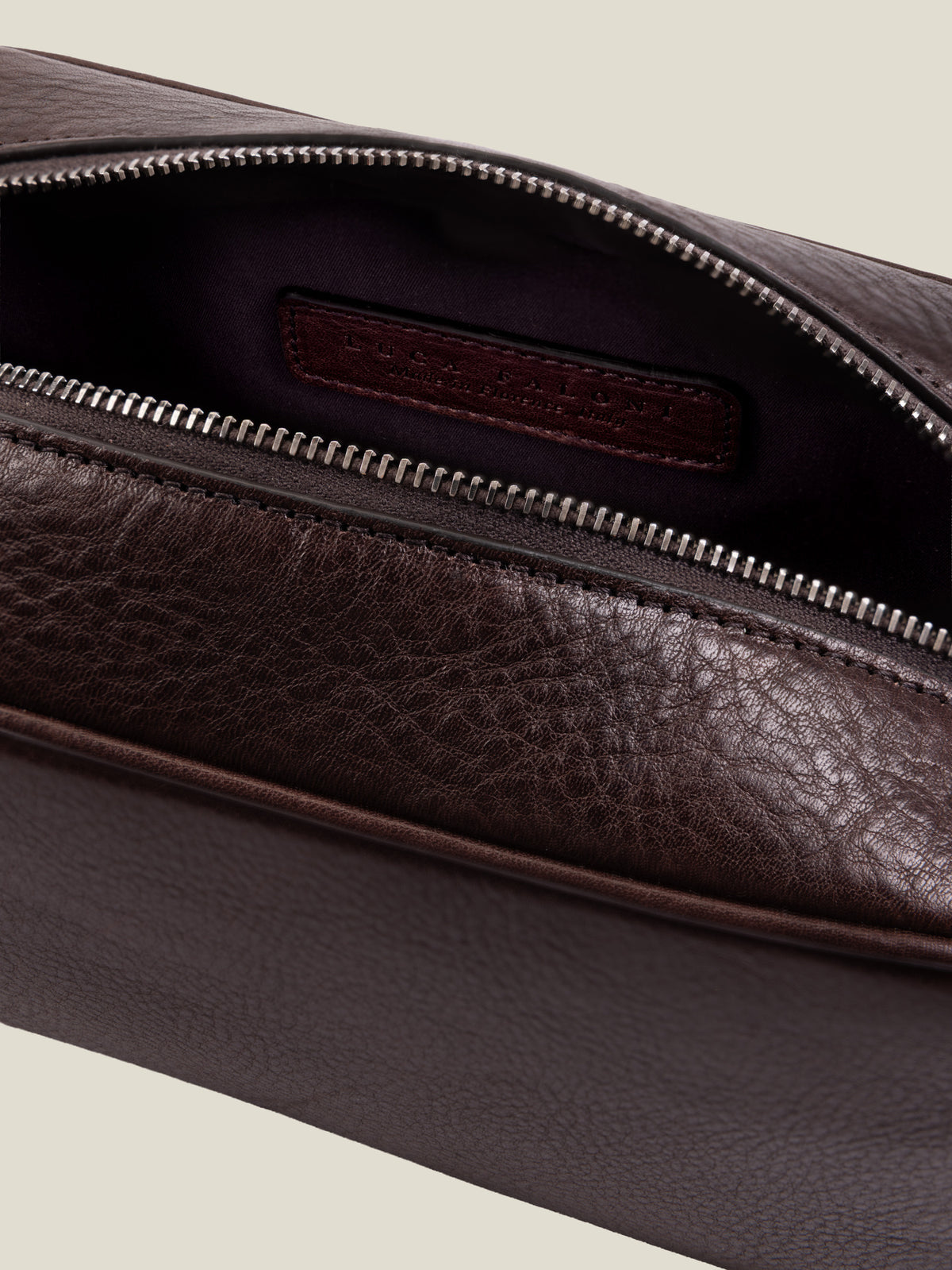 Close-up of the chocolate brown leather wash bag, showing the open silver zipper and water-resistant technical lining.
