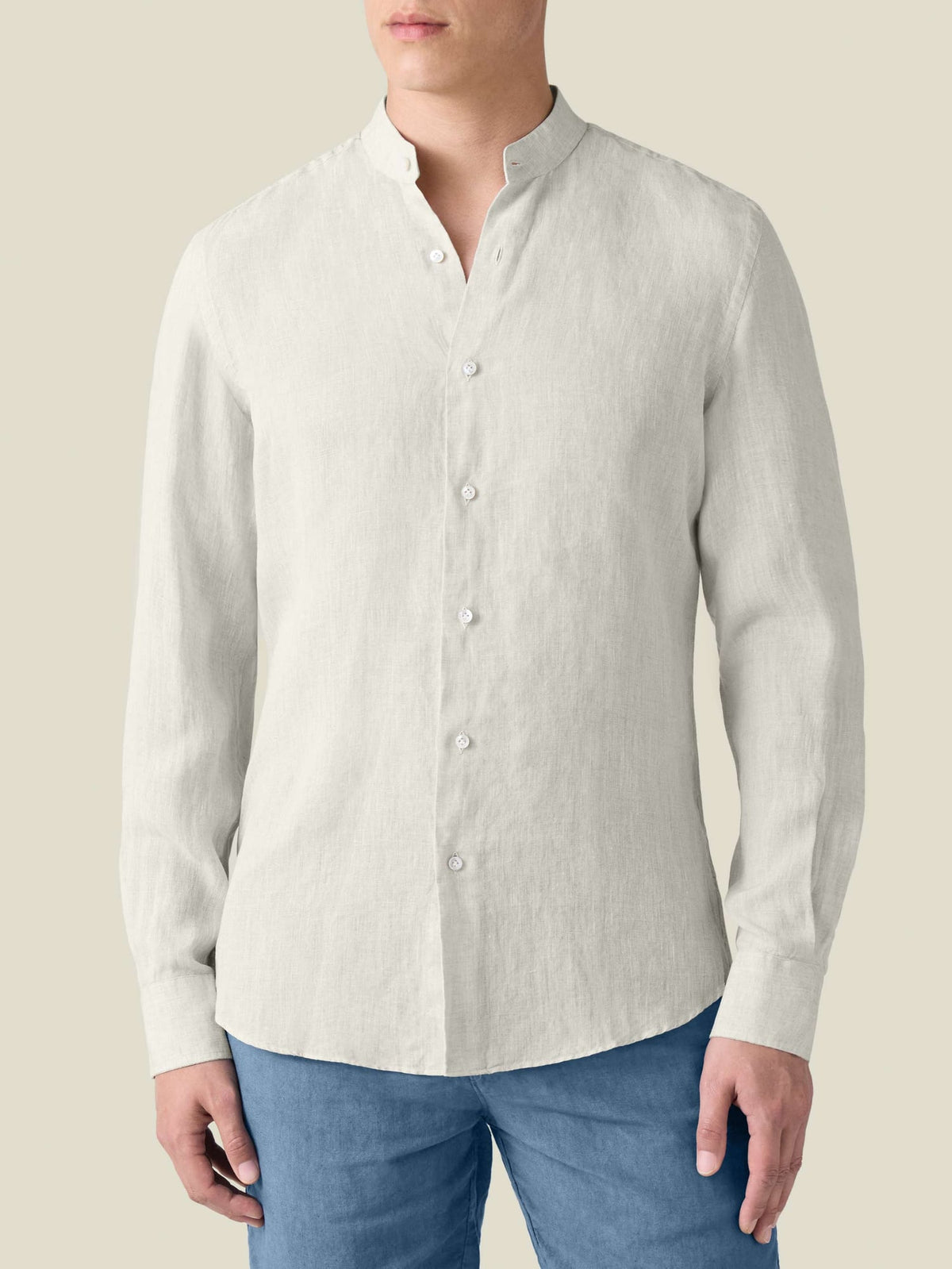 Front view of the sand Versilia Linen Shirt with a band collar, worn by a model and paired with blue trousers.