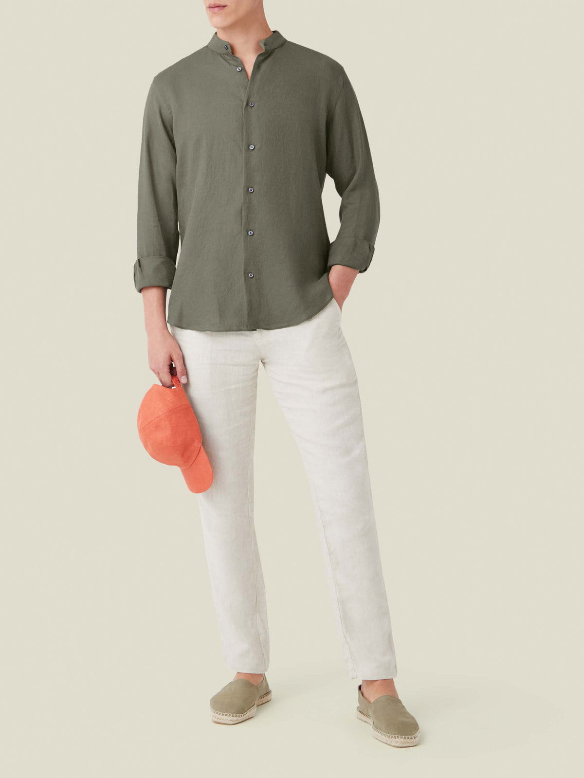 Khaki green Versilia Linen Shirt with a band collar, worn by a model with white trousers and an orange cap.