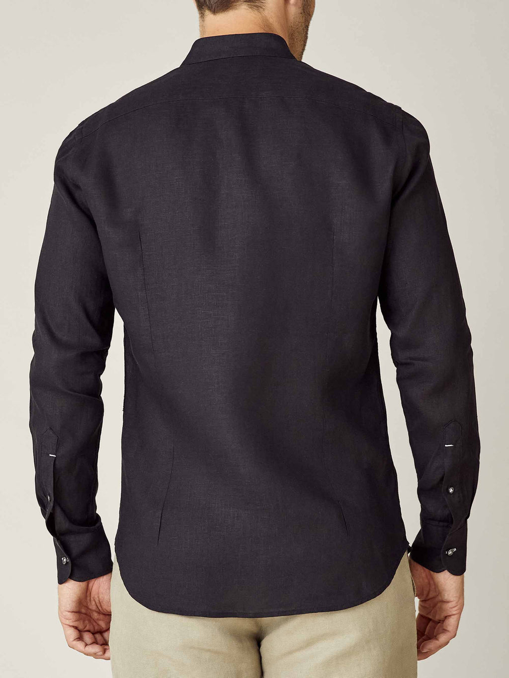 Back view of the black Versilia Linen Shirt with a band collar, worn by a model with beige trousers.