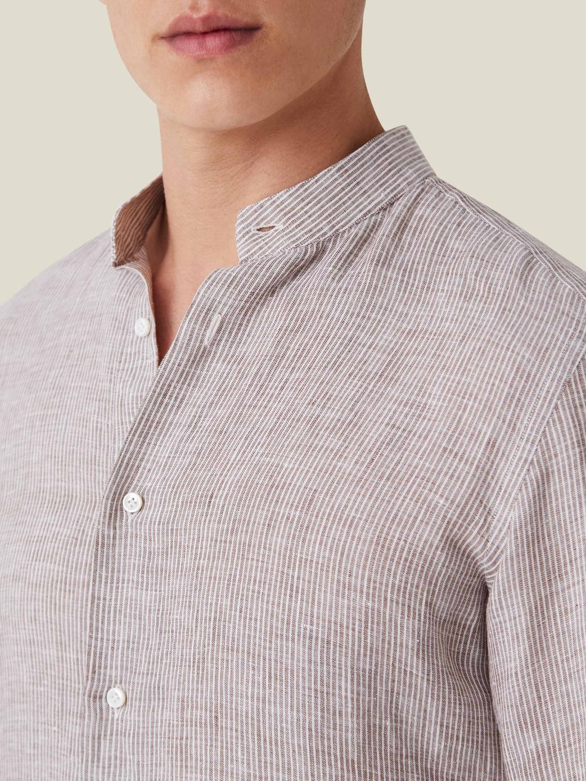 Close-up of the nocciola brown striped Versilia linen shirt with a band collar, worn by a model.