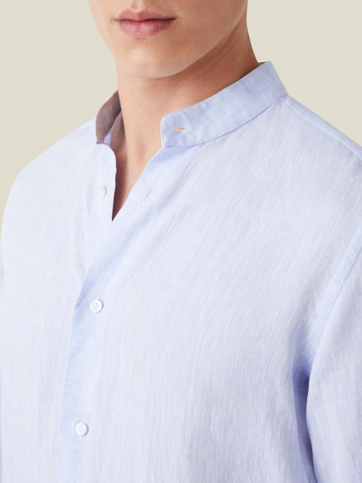 Close-up of the sky blue Versilia Linen Shirt with a band collar and mother of pearl buttons, worn by a model.