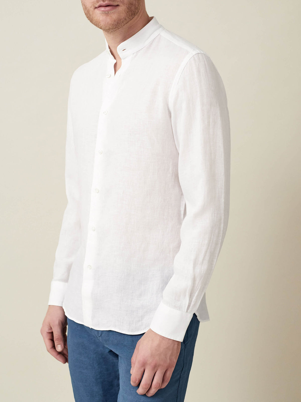 White Versilia Linen Shirt with a band collar, worn by a model and styled with blue trousers.