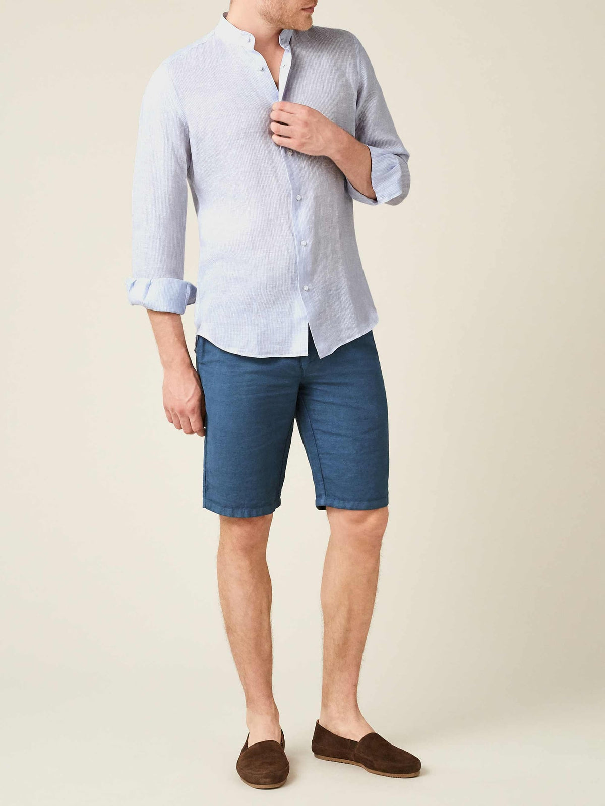 Striped sky blue linen shirt with a band collar and rolled sleeves, paired with blue shorts.