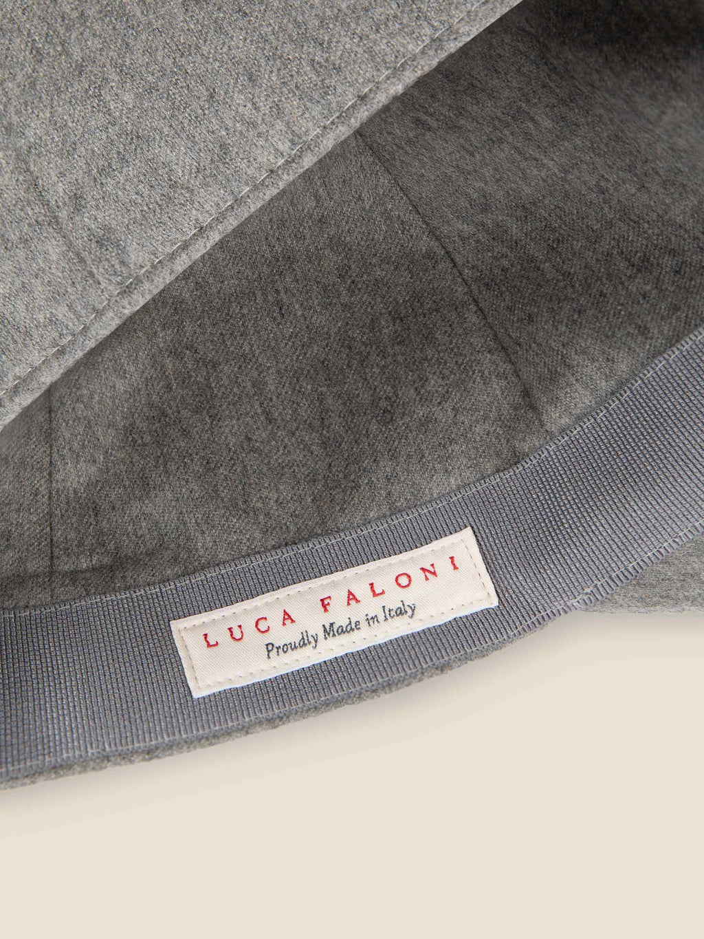 Close-up of the light grey cashmere baseball cap's interior, showing the Luca Faloni 'Proudly Made in Italy' label.