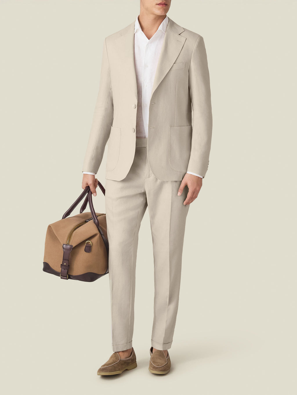 Full-length view of a model wearing the Luca Faloni sand linen blazer and matching trousers, holding a travel bag.
