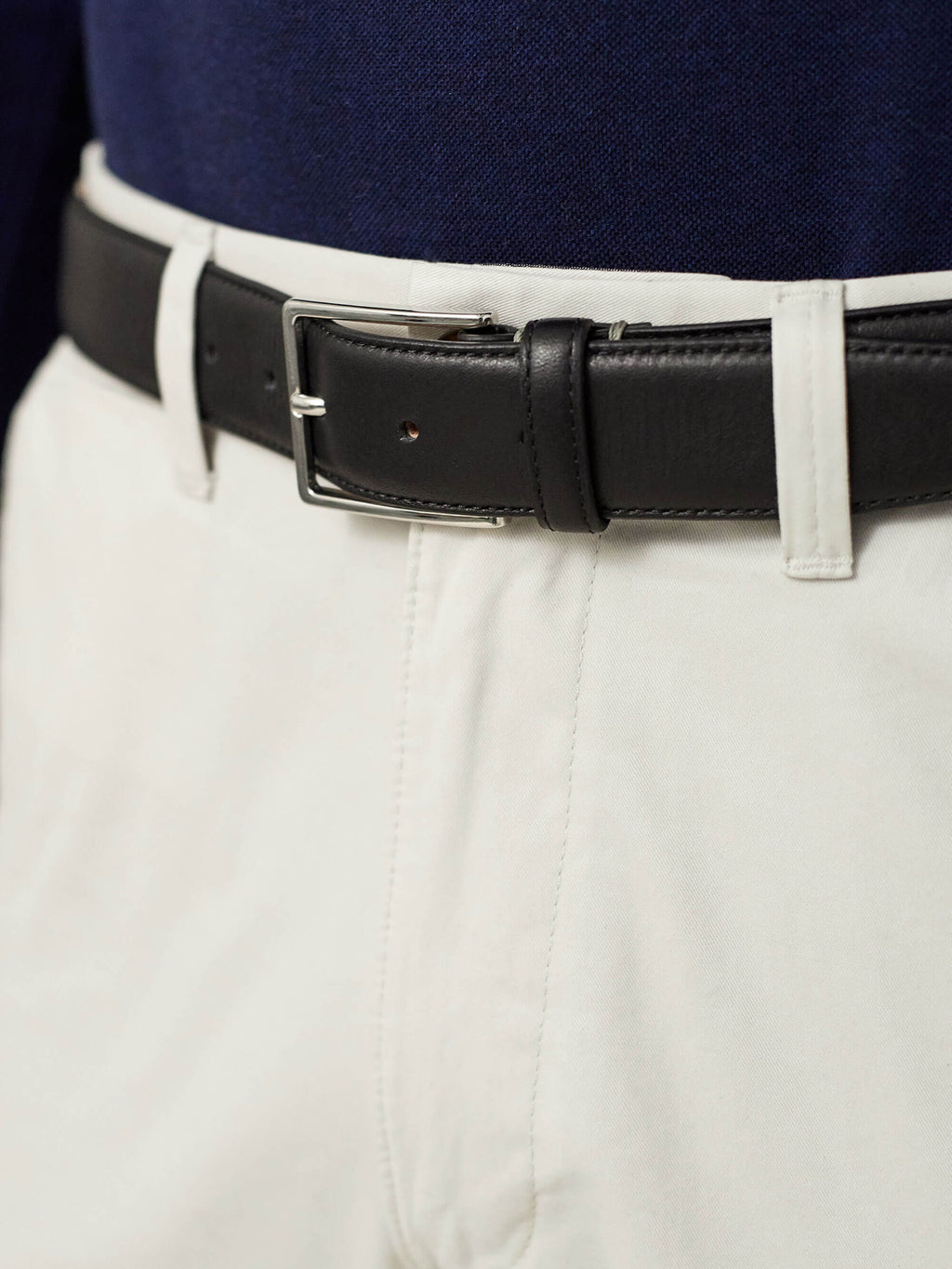 A close-up of the Black Calf Leather Belt with a silver buckle, worn by a model with white trousers and a navy top.