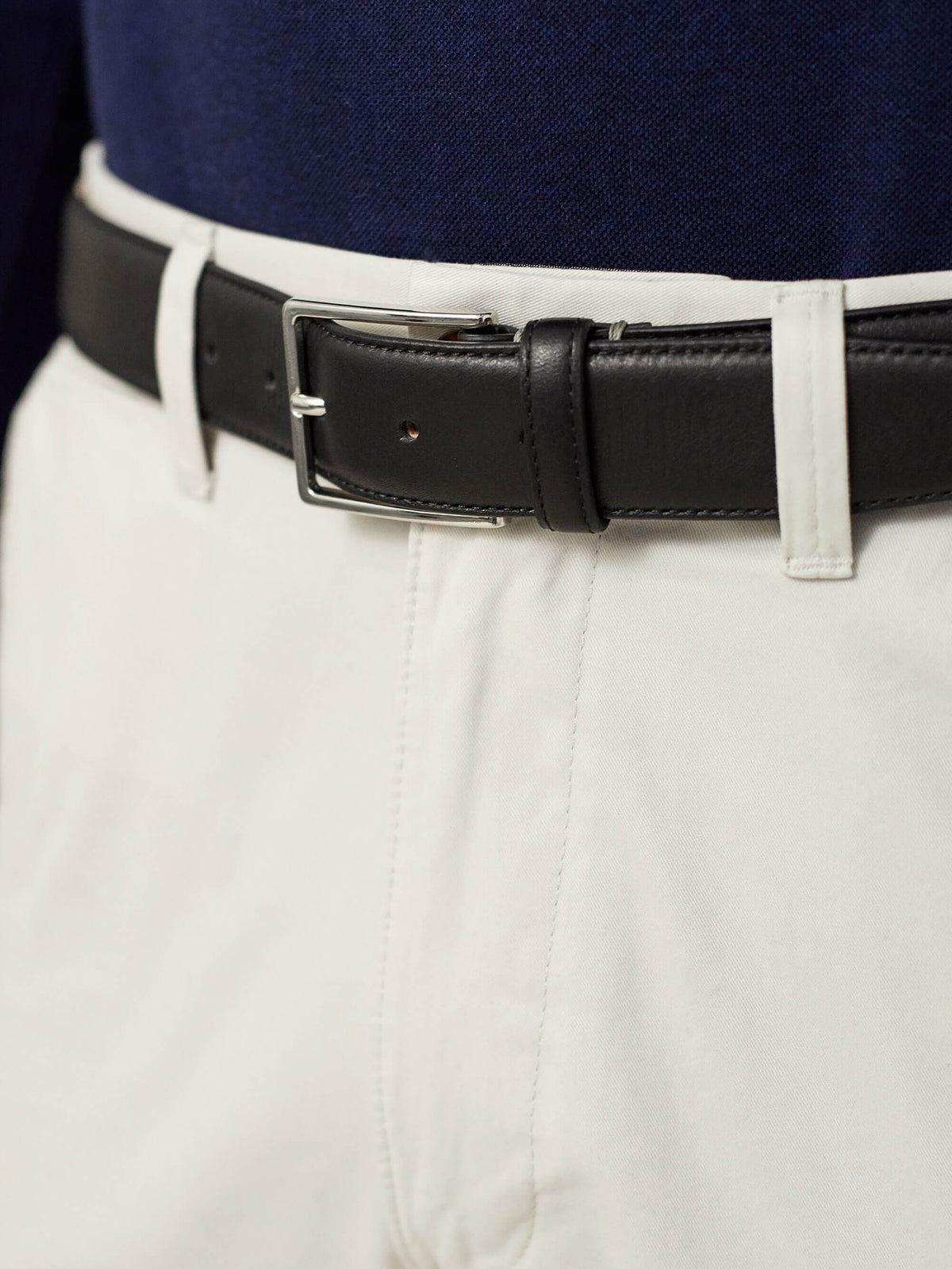 A close-up of the Black Calf Leather Belt with a silver buckle, worn by a model with white trousers and a navy top.