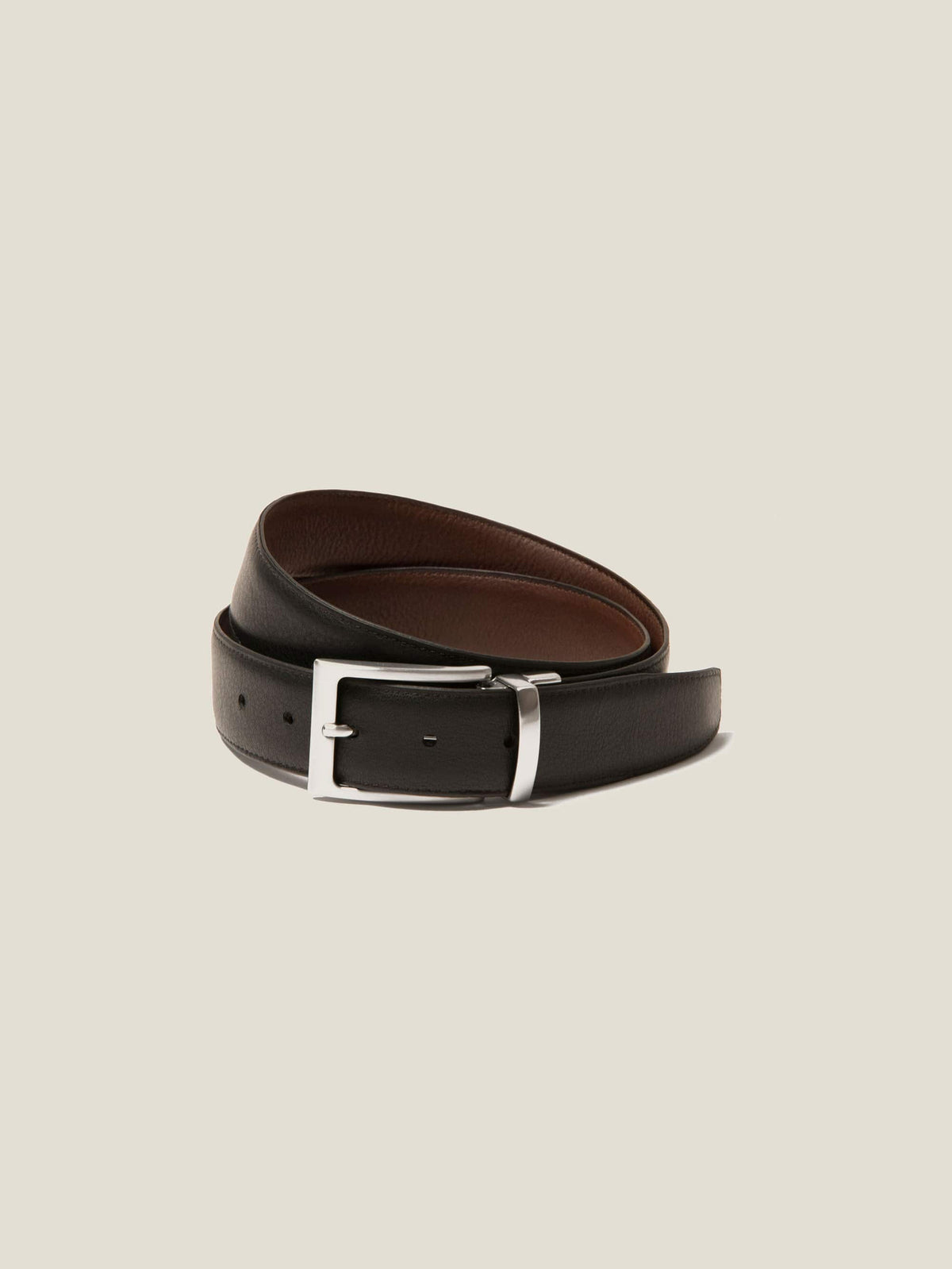 A reversible calf leather belt in black and brown, coiled with the black side facing out, featuring a silver-tone buckle.