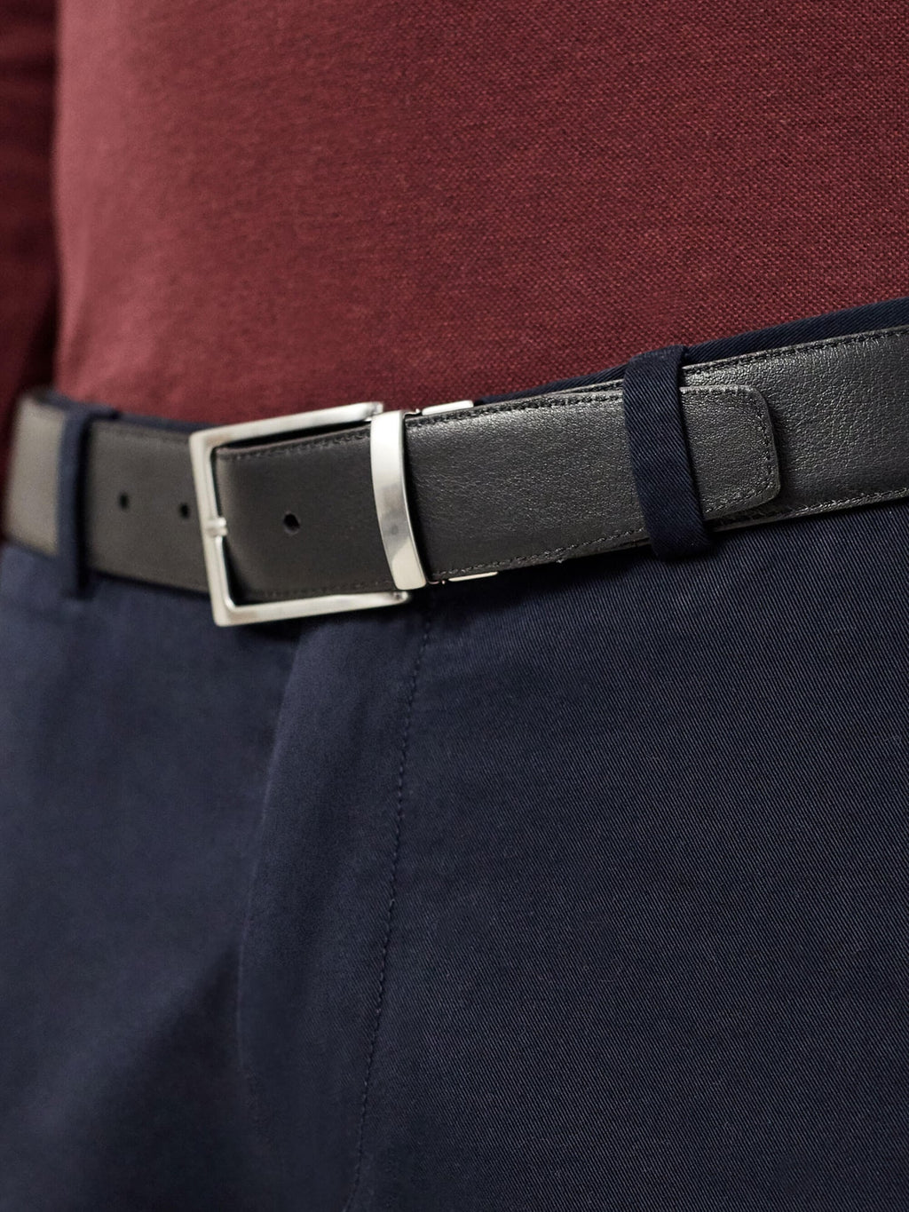 A close-up of the Luca Faloni Reversible Calf Leather Belt in black, styled with navy trousers and a burgundy shirt.