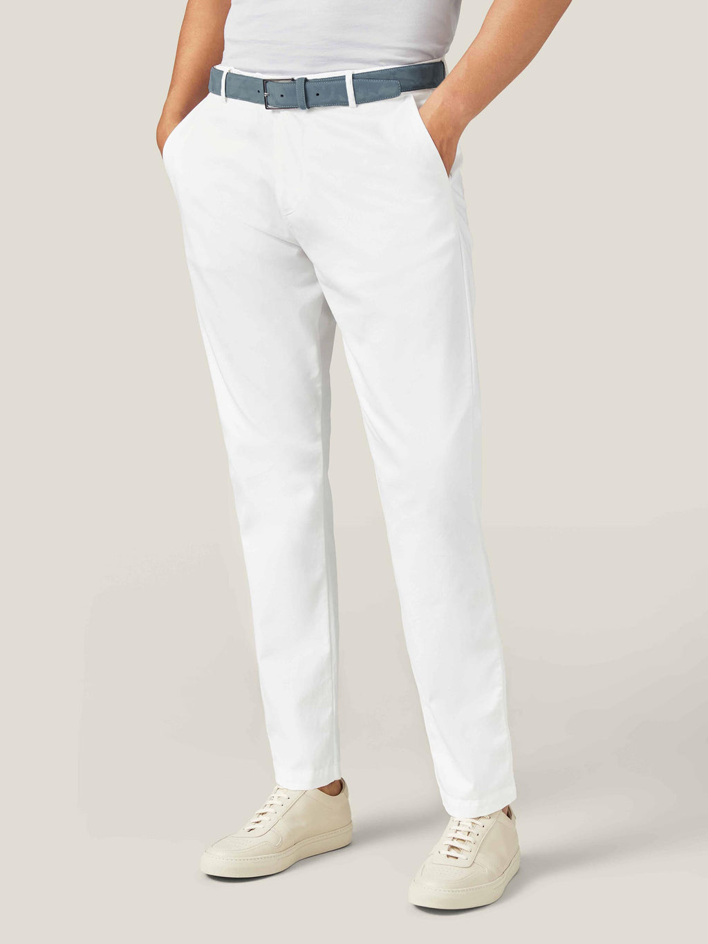 A model wears the Luca Faloni Steel Blue Nubuck Belt with white trousers and cream leather sneakers.