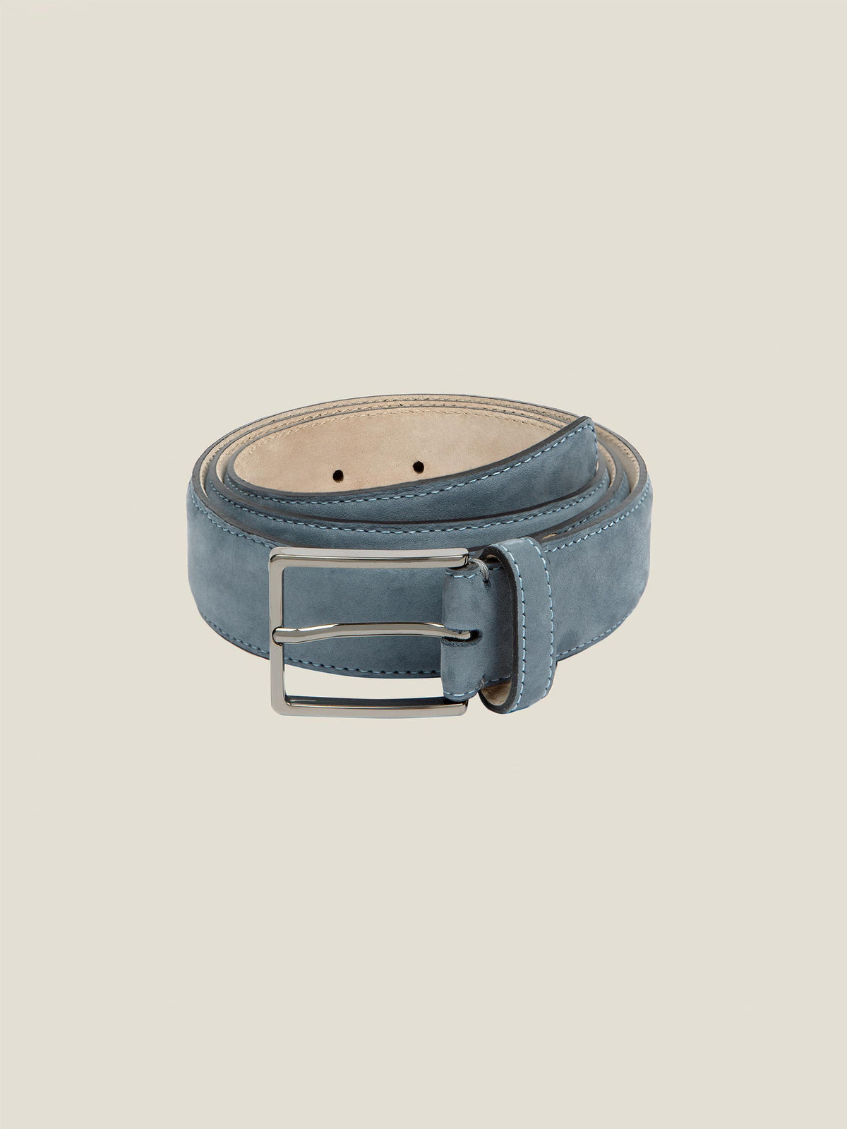 A coiled Luca Faloni Nubuck Belt in Steel Blue, showcasing its soft, velvety texture and classic silver-tone buckle.