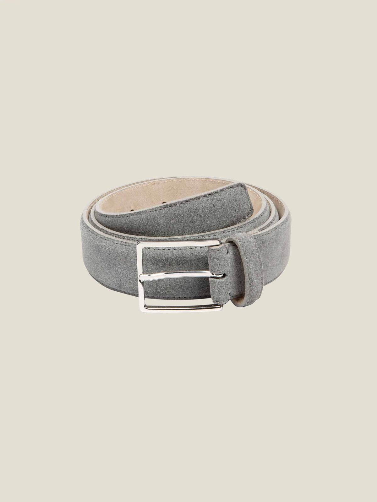 A coiled Classic Suede Belt in French Blue, showing its full length and silver buckle against a studio background.