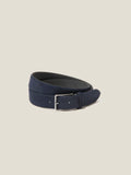The Luca Faloni Classic Suede Belt in navy blue, coiled to showcase its soft suede texture and silver-finish buckle.