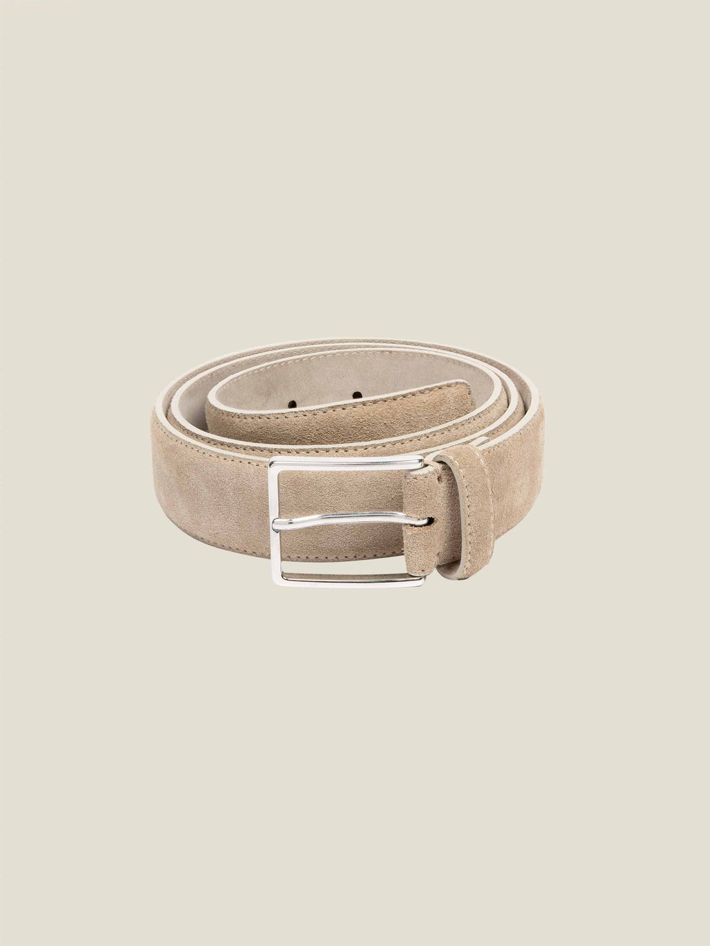 A sand-coloured Classic Suede Belt, coiled to display its soft texture and the polished silver-tone buckle.