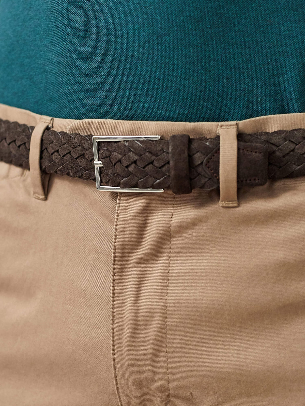 A close-up of a model wearing the Dark Brown Woven Suede Belt with beige chinos and a teal polo shirt.