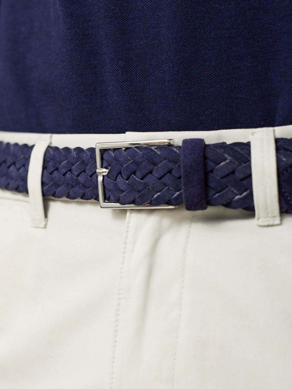 Close-up of Luca Faloni's navy blue woven suede belt with a silver buckle, styled with off-white trousers and a navy polo.