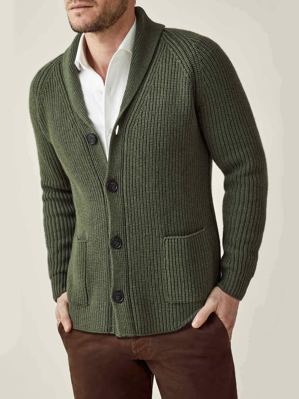 Model wearing the chunky knit cardigan in hunting green with a shawl collar, layered over a white shirt and brown trousers.