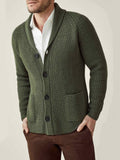 Model wearing the chunky knit cardigan in hunting green with a shawl collar, layered over a white shirt and brown trousers.