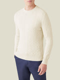 A man models the Luca Faloni Cable Knit jumper in ivory cashmere, paired with dark navy trousers.