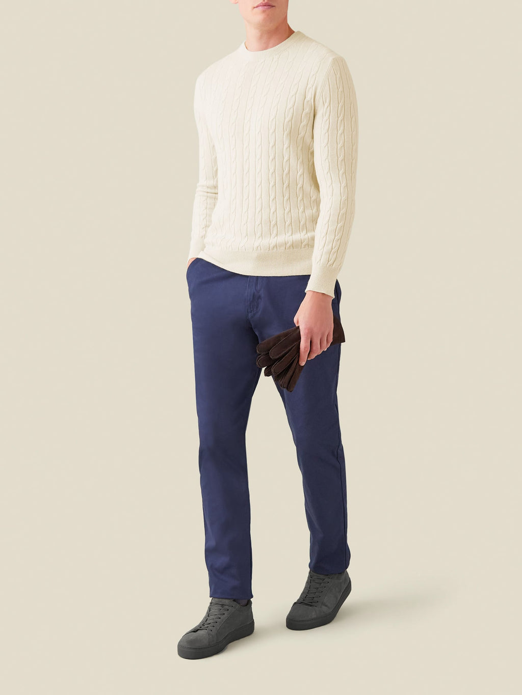 Model wears the Luca Faloni ivory cashmere cable knit sweater with navy trousers and dark grey sneakers.
