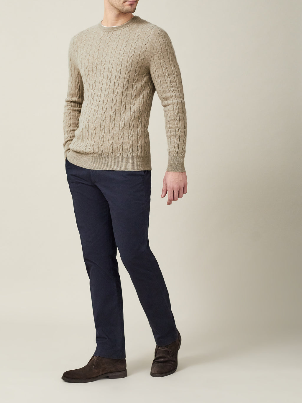 A front view of a model wearing the Luca Faloni Cashmere Cable Knit in Camel Beige with navy trousers and brown suede shoes.