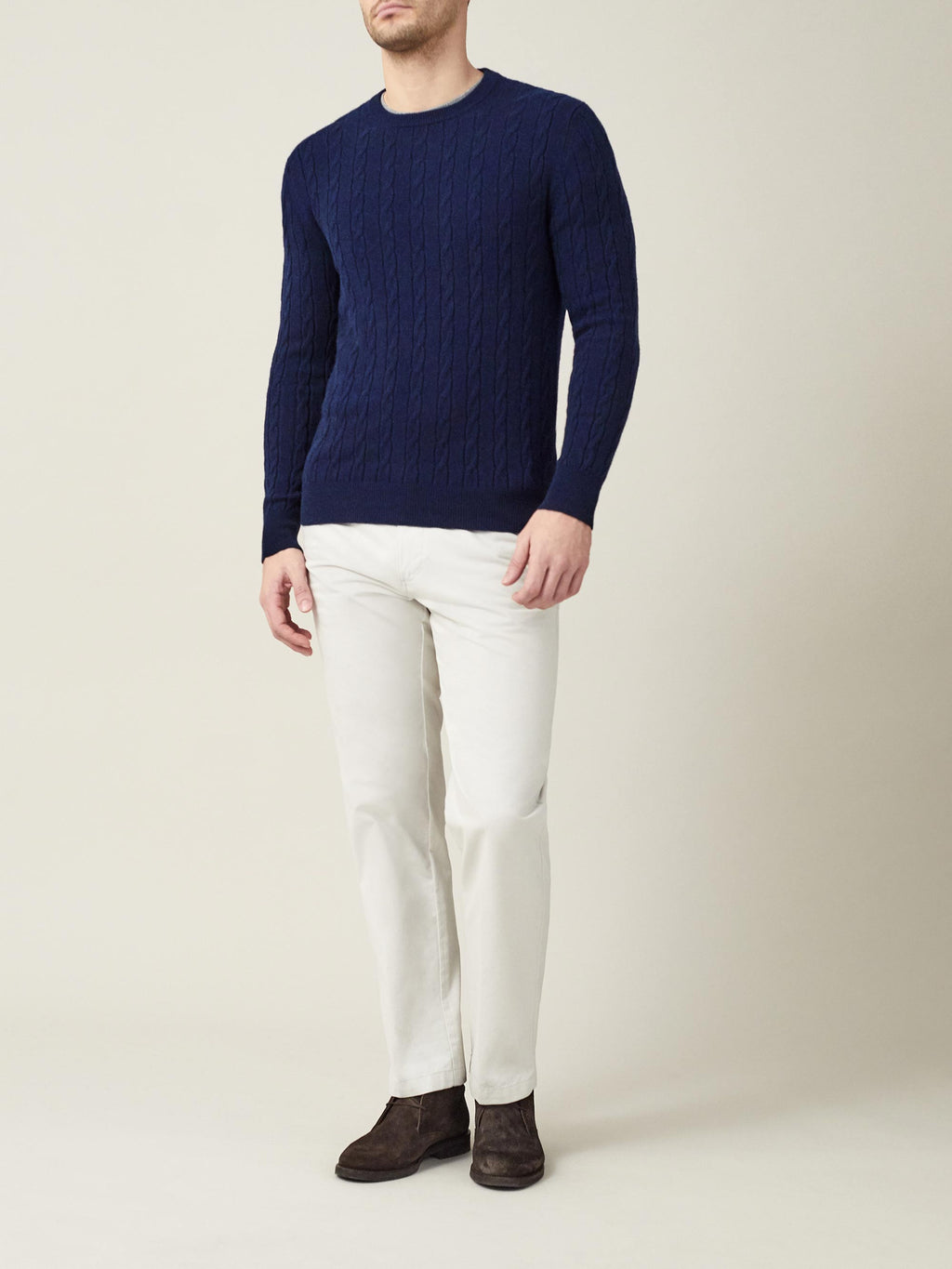 Model seen from the front wearing the Midnight Blue Cashmere Cable Knit sweater with off-white trousers and dark brown boots.