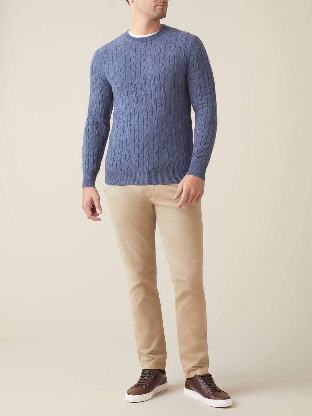 Full-length shot of a model wearing the Sialia Blue Cashmere Cable Knit jumper with beige chinos and brown leather trainers.