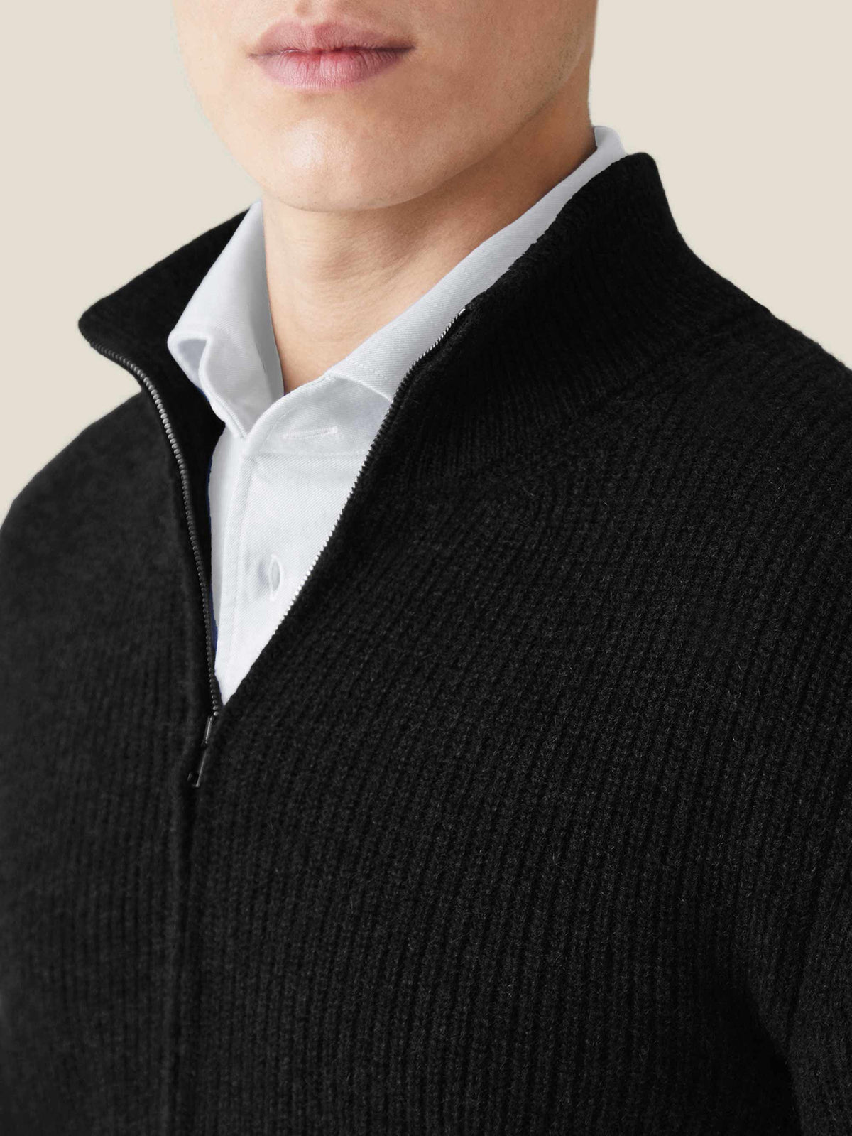 Close-up of a man wearing a black chunky knit cashmere zip cardigan, showing the ribbed texture and high collar.