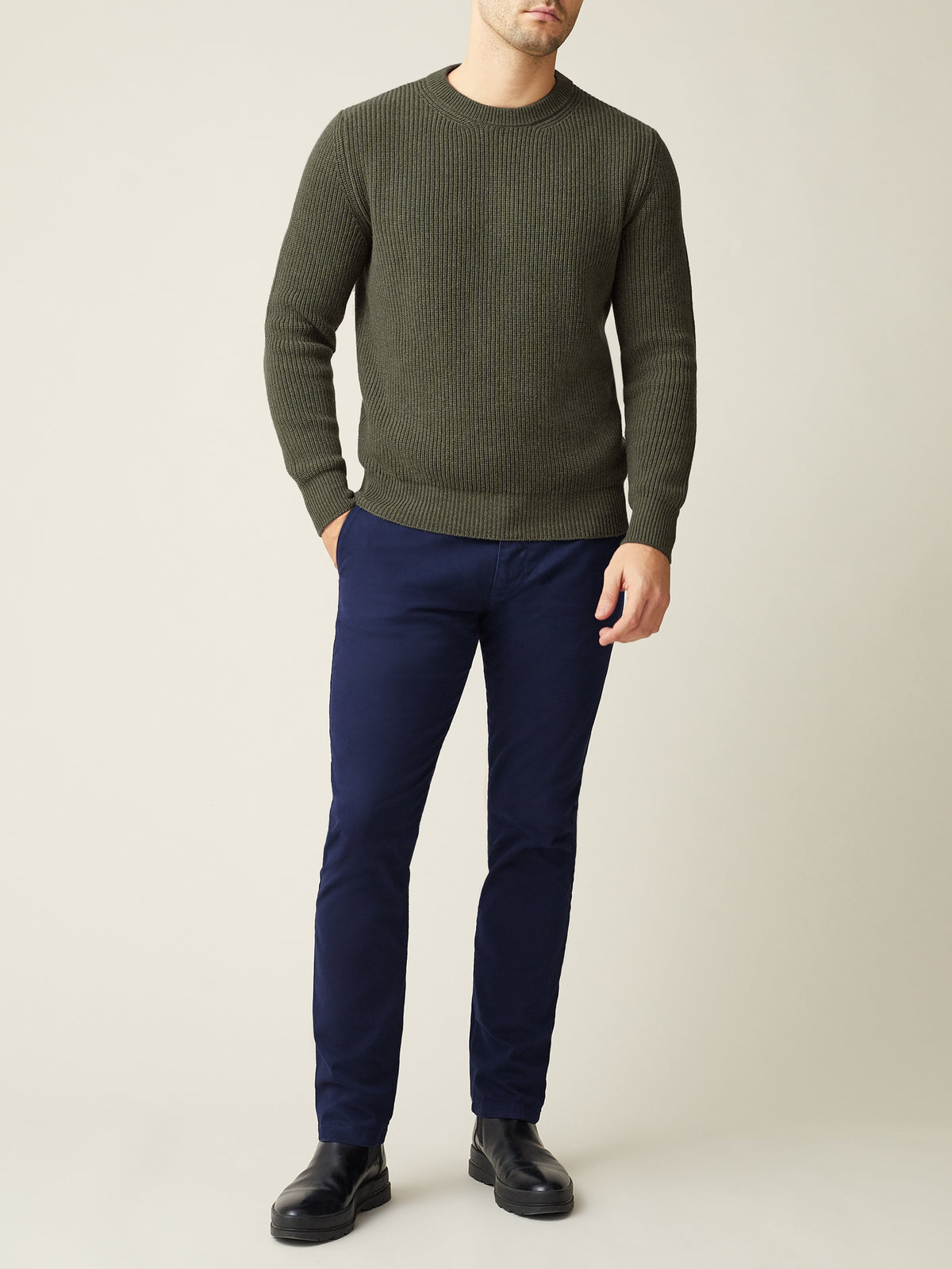 A man models the Chunky Knit Crew Neck in Hunting Green, a ribbed cashmere sweater, styled with dark navy trousers.
