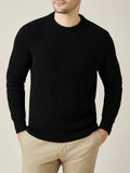 Front view of a model wearing the black Chunky Knit Crew Neck sweater with beige trousers, with his hands in his pockets.