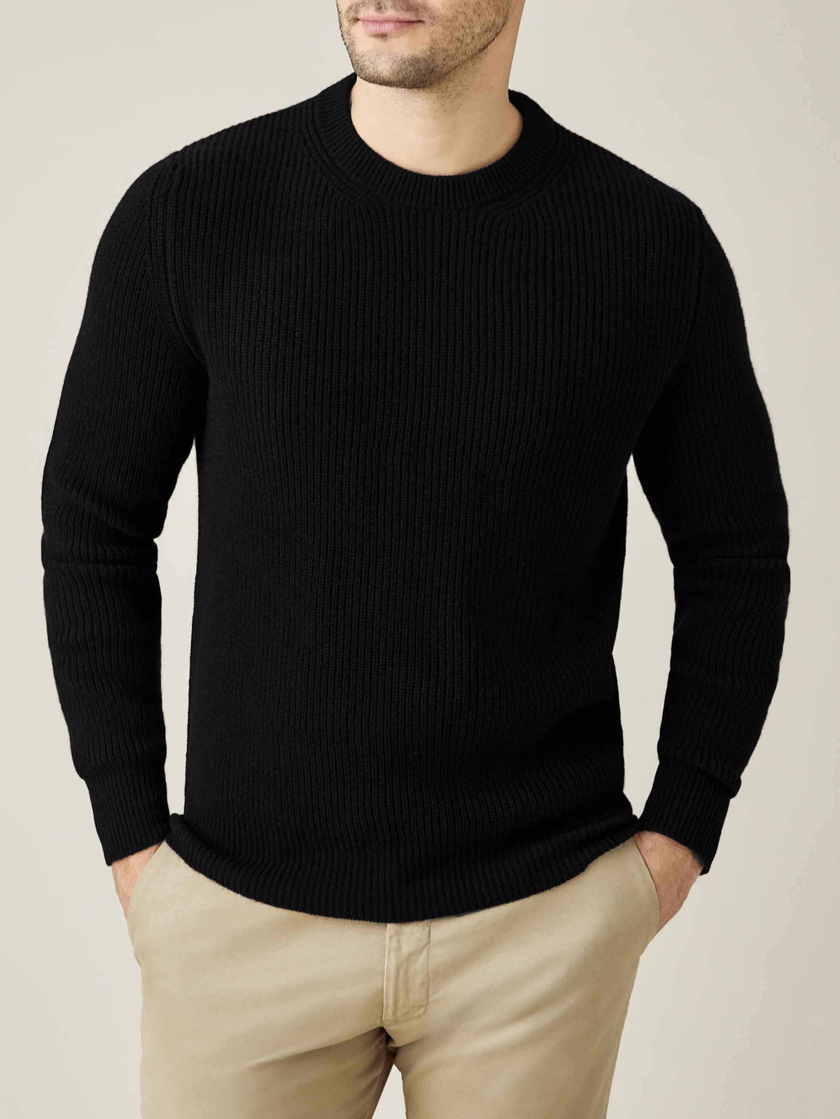 Front view of a model wearing the black Chunky Knit Crew Neck sweater with beige trousers, with his hands in his pockets.