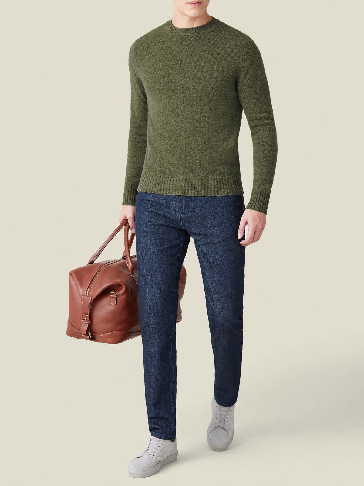 Model wears Luca Faloni's Country Crew Neck in Hunting Green with dark jeans, white sneakers, and a brown leather bag.