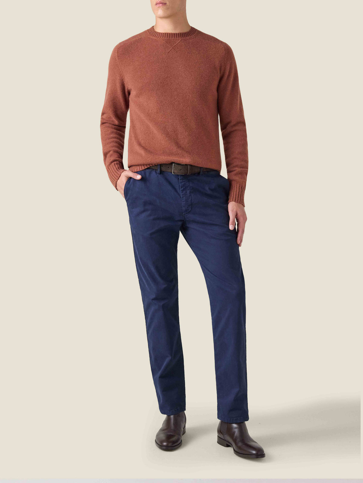 A model wears the Luca Faloni Rust Cashmere Country Crew Neck paired with navy blue trousers and dark brown leather boots.