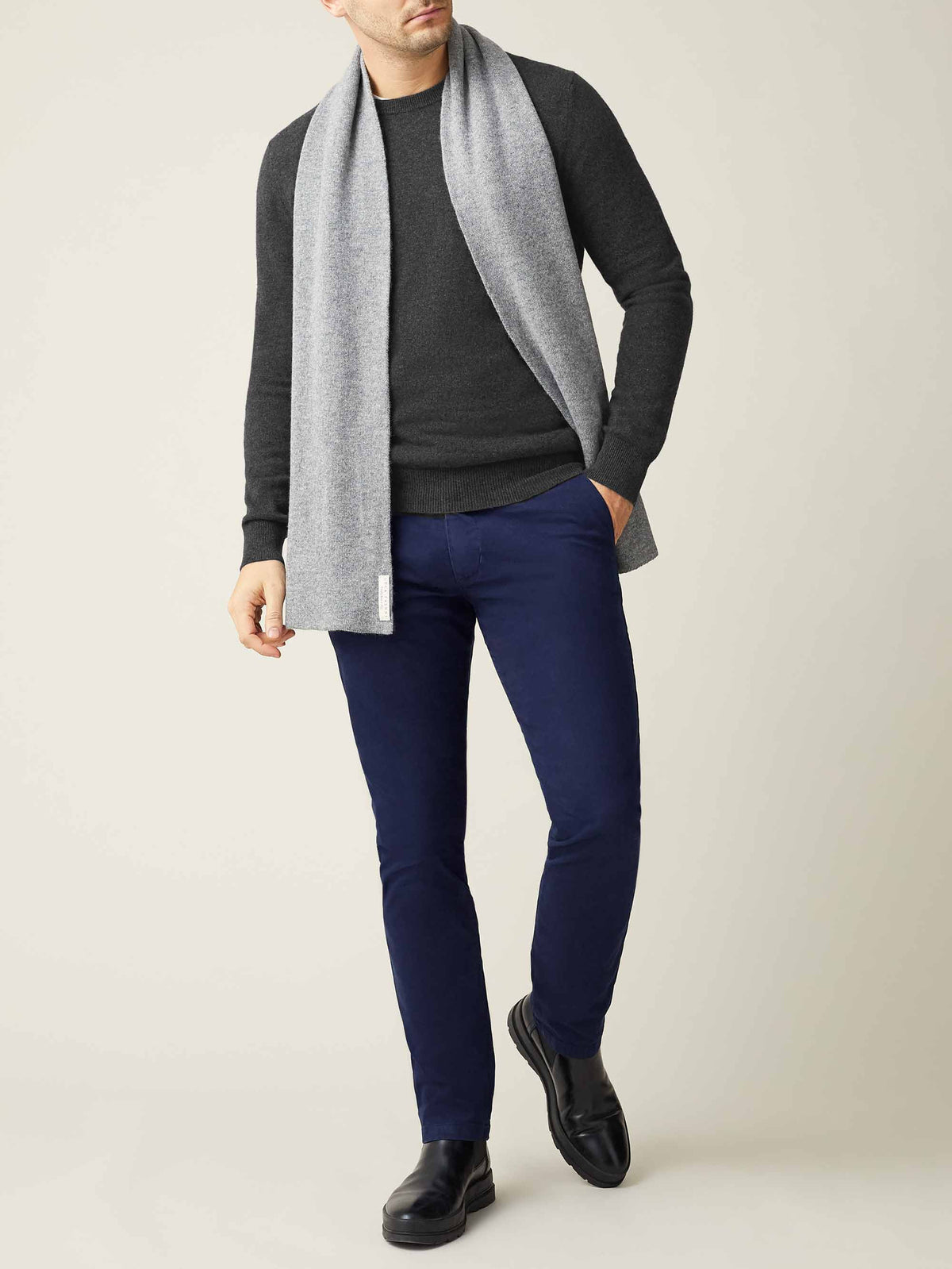 A model wears the Luca Faloni charcoal grey cashmere crew neck, styled with a light grey scarf and dark navy trousers.