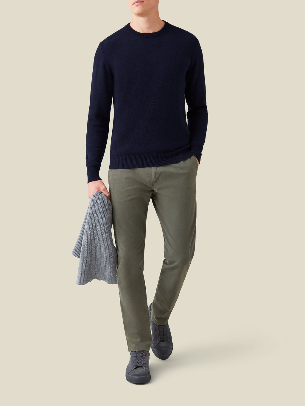 Model wearing the Midnight Blue Cashmere Crew Neck with olive chinos and dark trainers, carrying a grey sweater.
