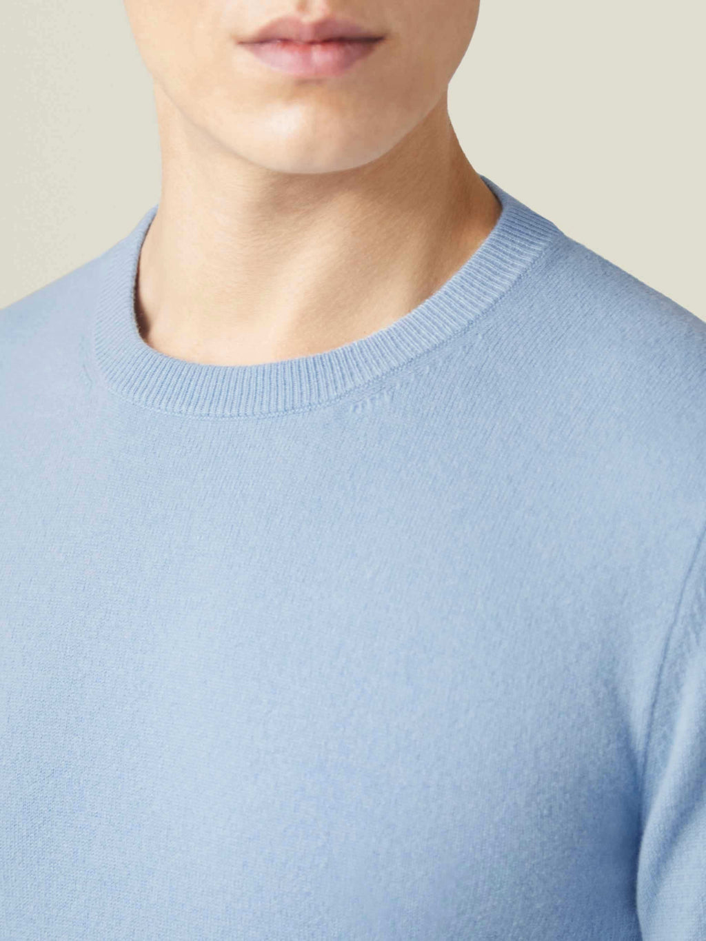 A close-up of a model wearing the sky blue cashmere crew neck, showcasing the sweater's ribbed neckline and soft texture.