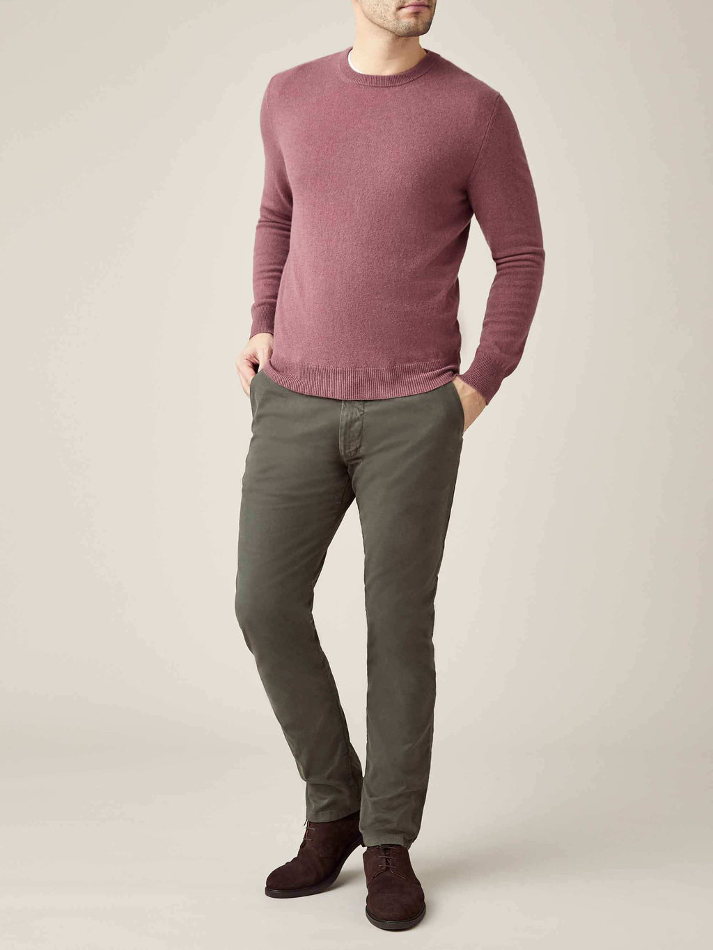 A male model wears the Luca Faloni men's cashmere crew neck in Desert Rose with olive trousers and brown shoes.