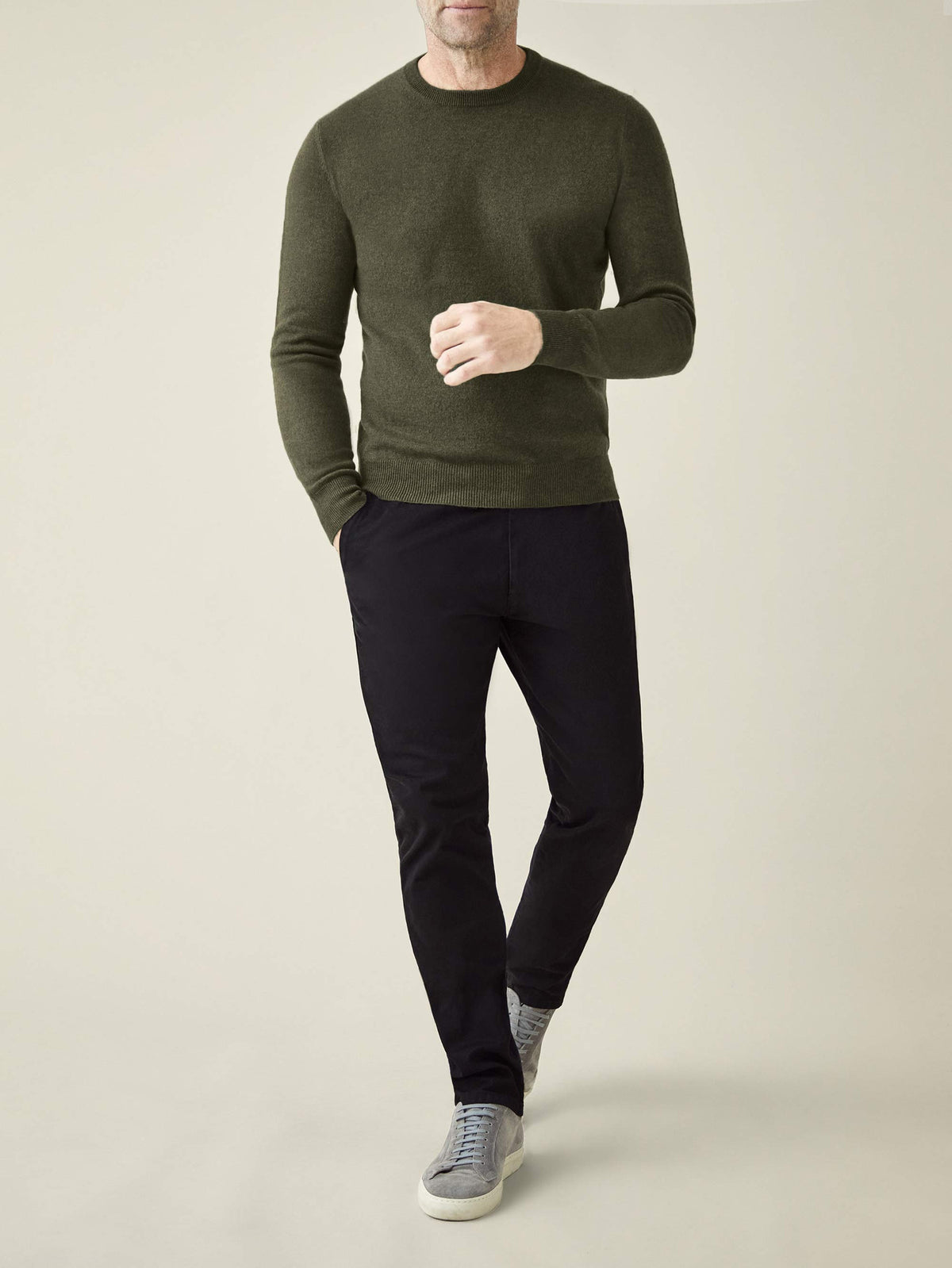 A man models the Luca Faloni Cashmere Crew Neck in Hunting Green, paired with black trousers, in a full-length front view.