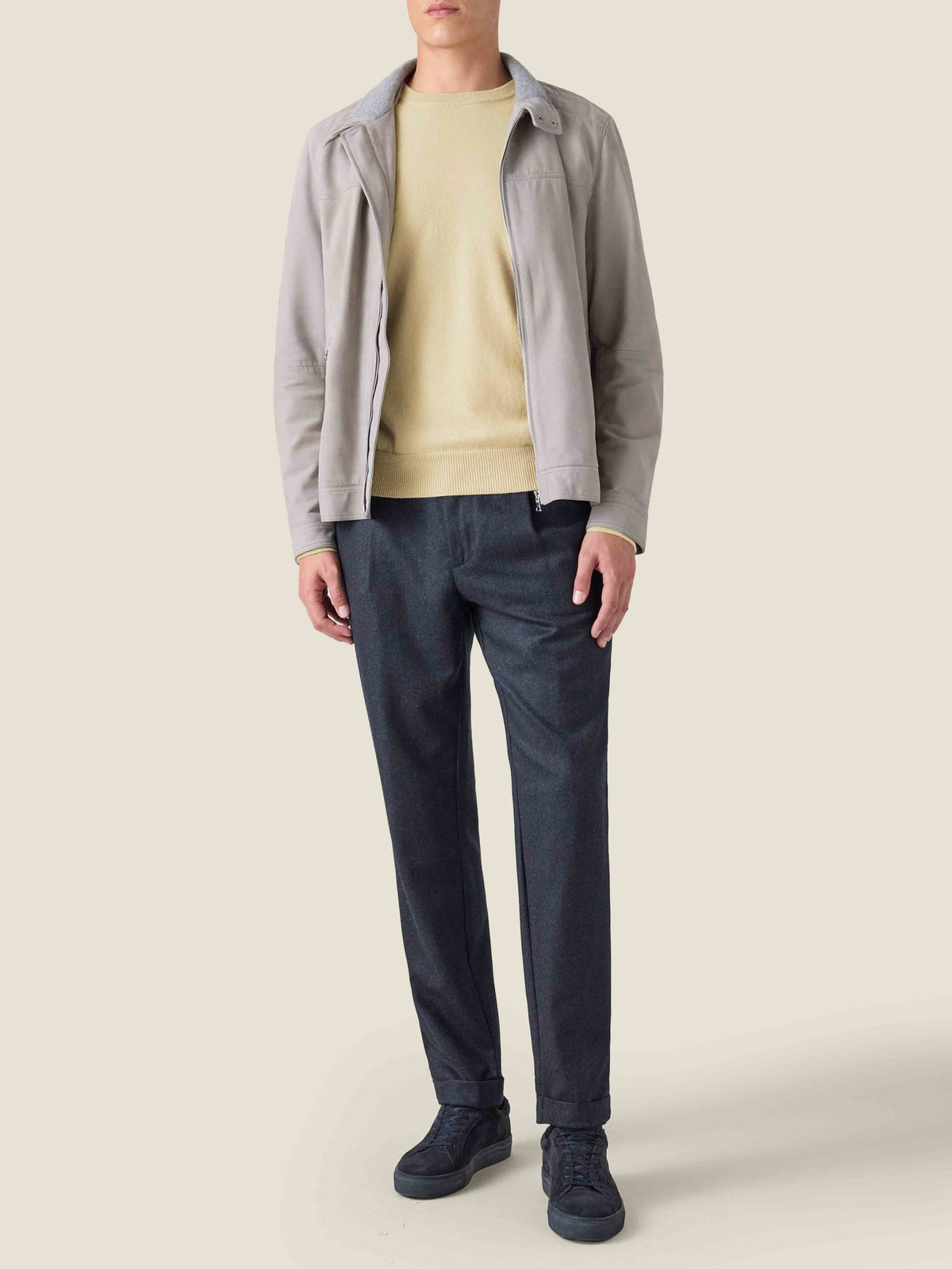 A model wears a yellow cashmere crew neck jumper layered under a light grey zip-up jacket with dark trousers.