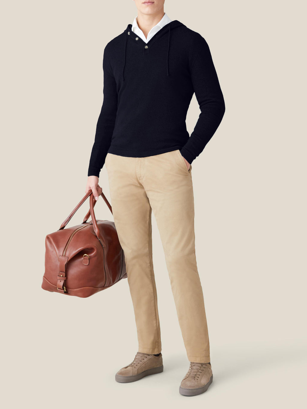 A model showcases the Midnight Blue Cashmere Hoodie, styled with beige chinos and a leather weekender bag for a travel look.
