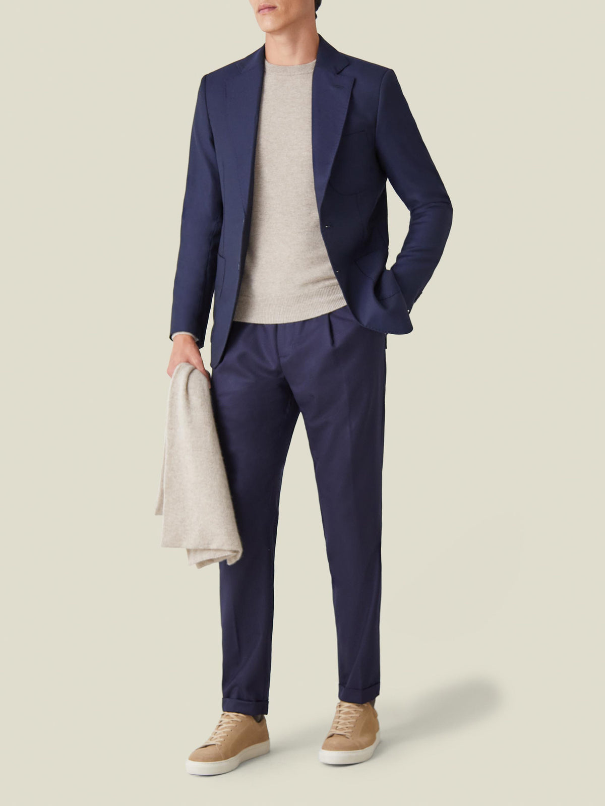 Front view of a model wearing the Navy Wool Travel Blazer with a beige top, matching trousers and tan sneakers.
