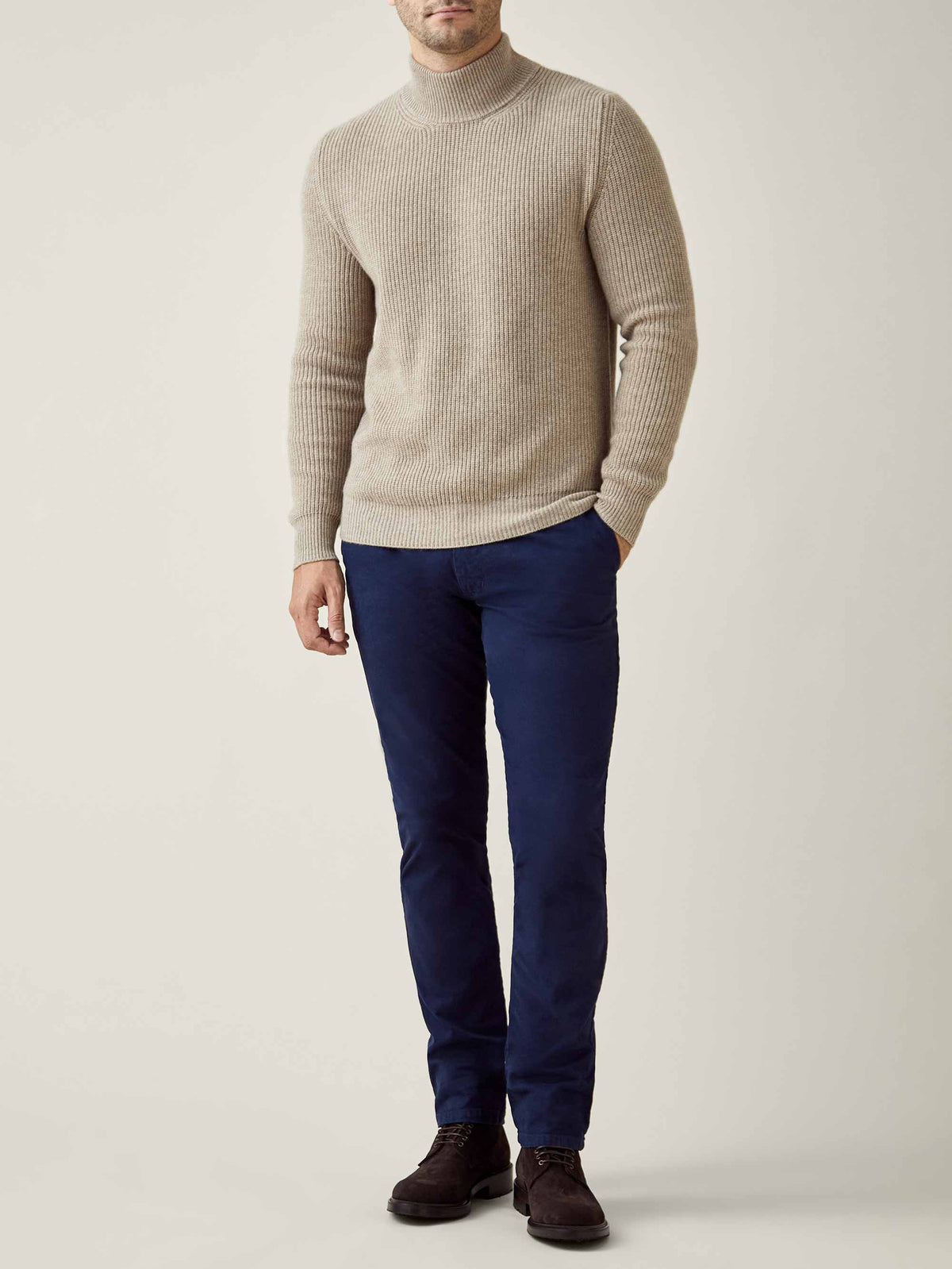 A front view of a model wearing the Chunky Knit Mock Neck in Camel Beige with navy trousers.