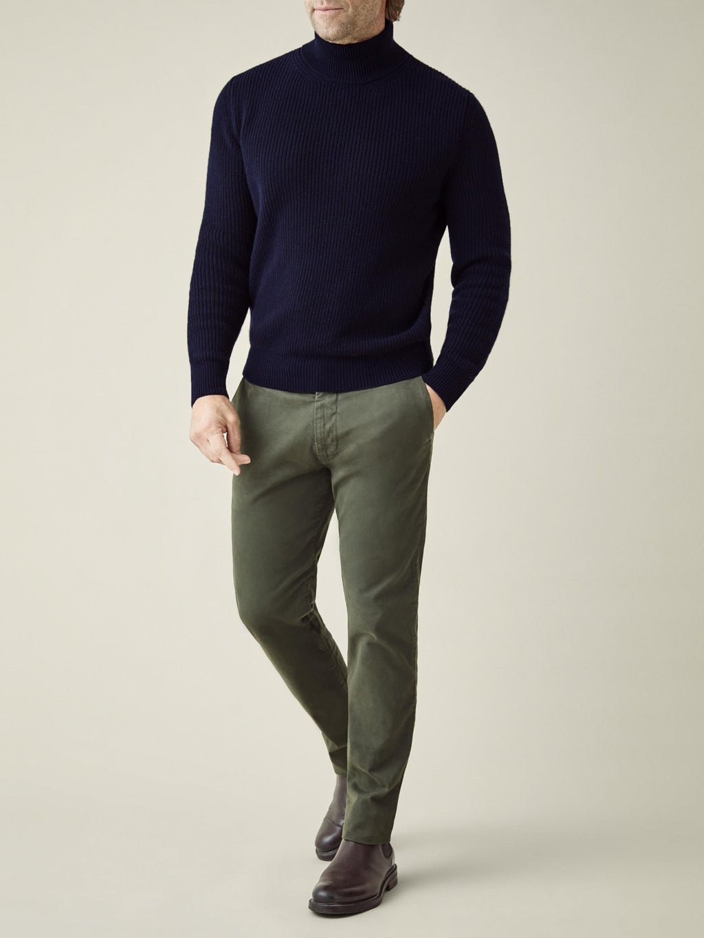 A front view of a model wearing the Chunky Knit Mock Neck in Midnight Blue with olive green trousers and brown boots.